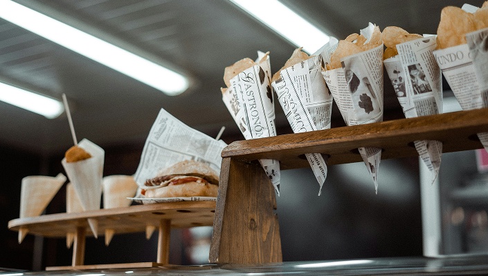 Snacks in Papiertüten und ein Sandwich in Holzhaltern auf einer Theke